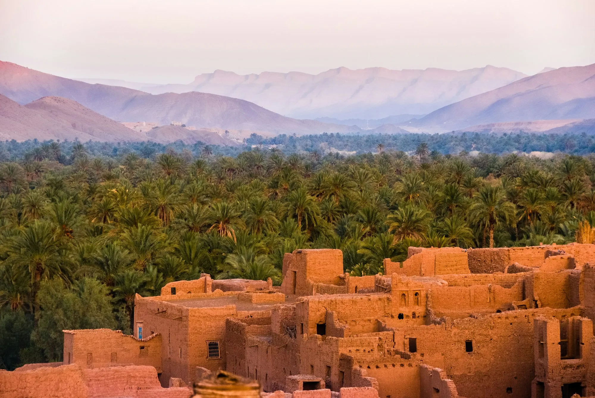 Earth-red kasbah walls among palm groves below the mountains